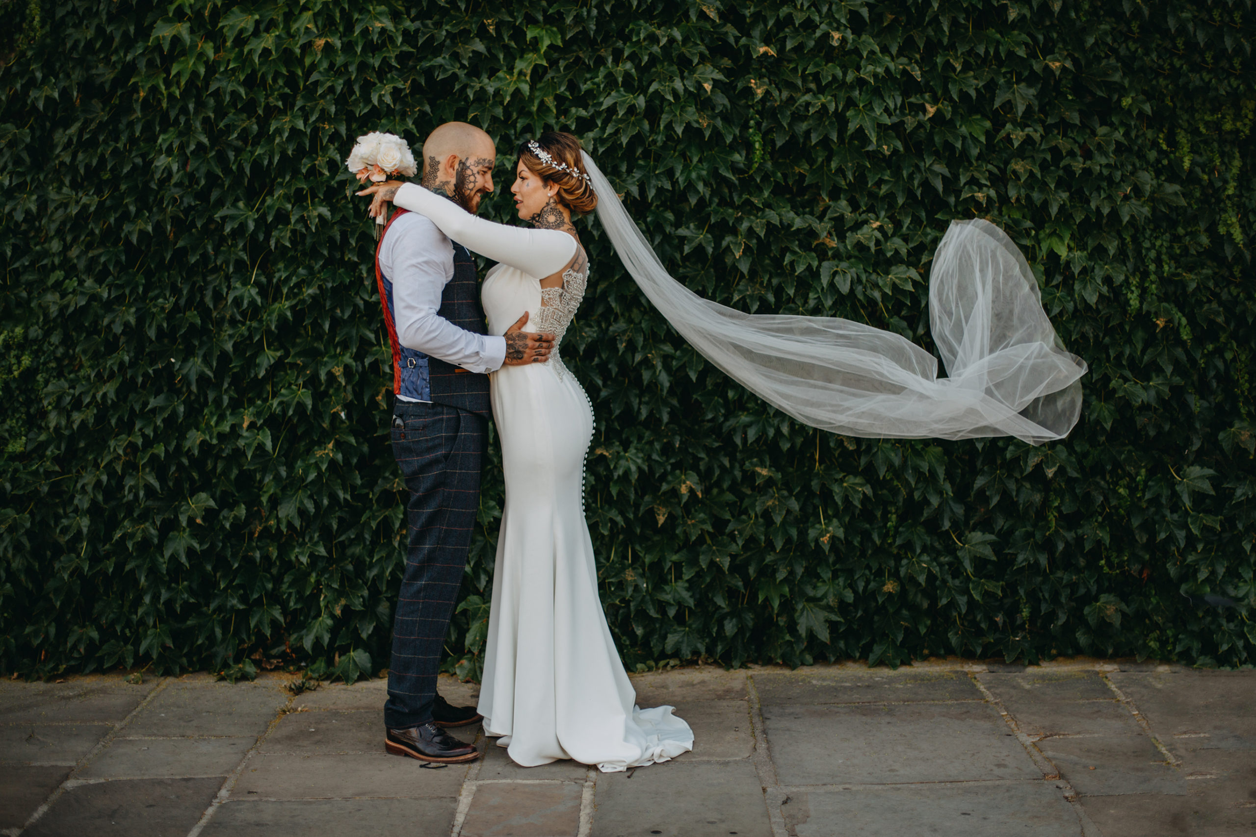 tattooed bride and groom wearing white wedding dress and veil in wind